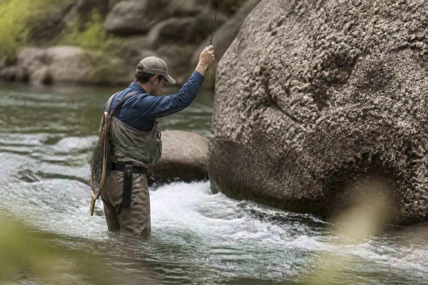 A fly angler standing close to a boulder holding the rod high while short line nymphing a narrow seam of fast pocket water