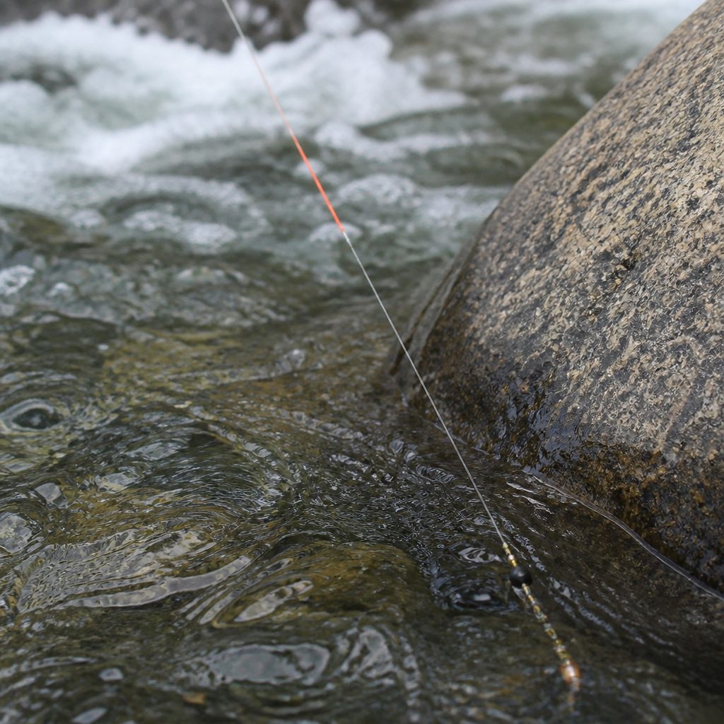 Close view of a leader with a coloured sighter section and two weighted nymphs entering fast clear water beside a boulder